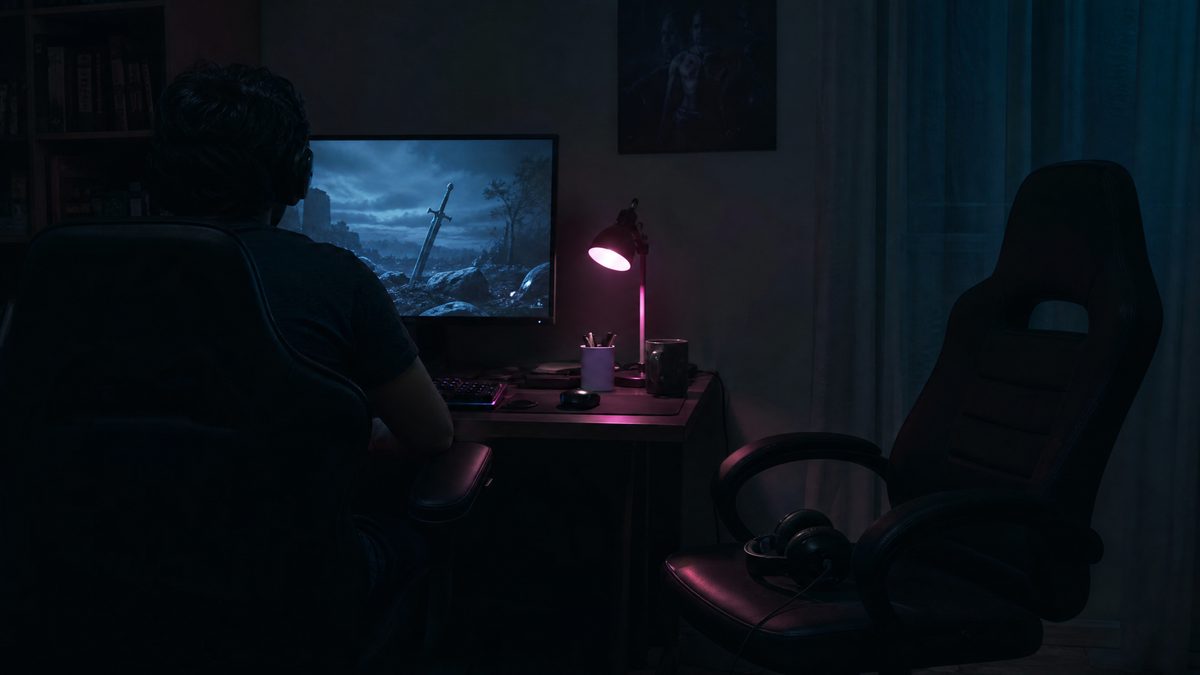 An empty second chair beside an occupied gaming desk at night with a spare unplugged headset